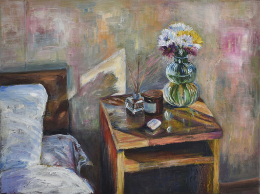 Settling In — a bedside table with daisies, a candle and a reed diffuser, beside a bed with the covers pushed back